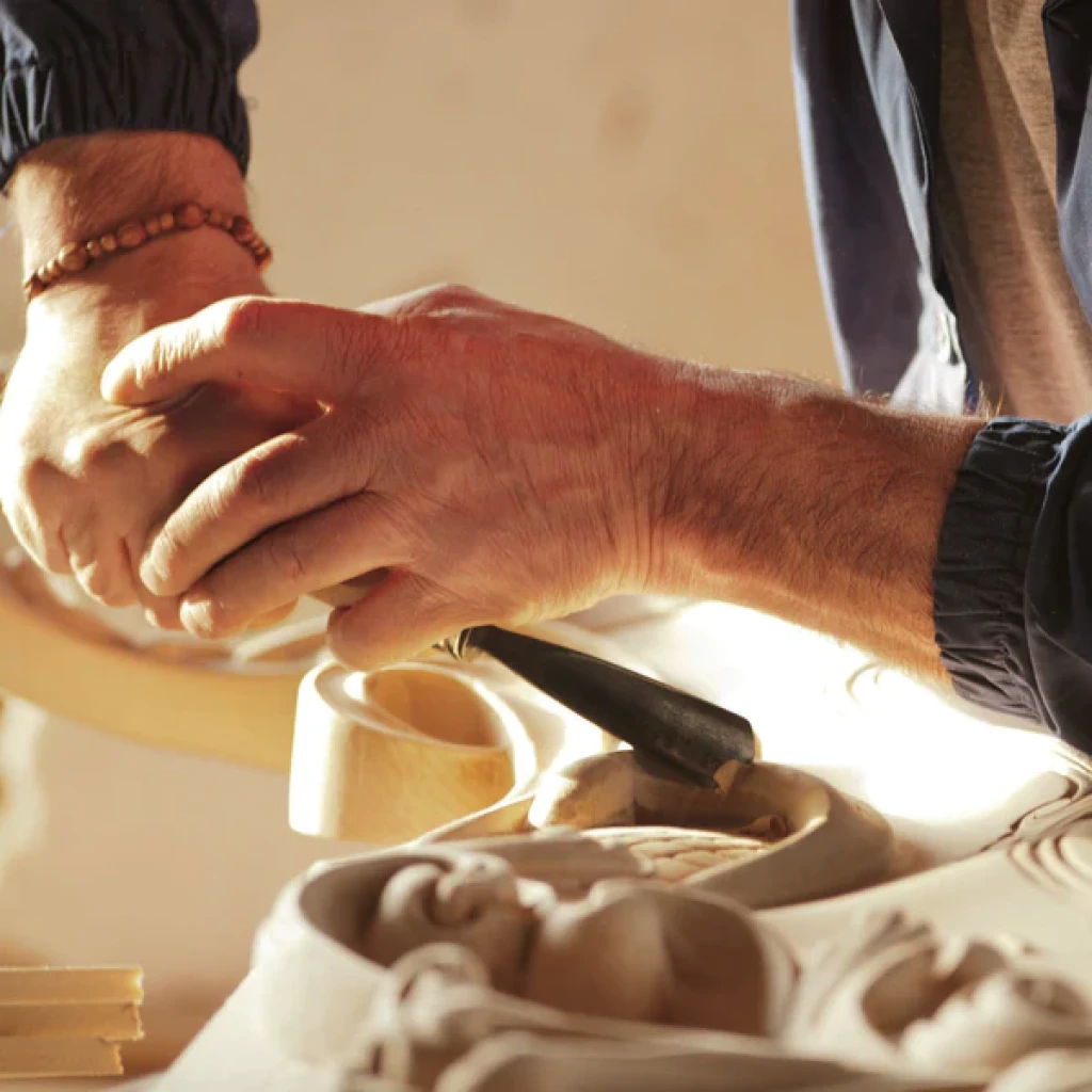 Close-up of artisan hands carving intricate patterns into wood, highlighting the precision and artistry of Italian craftsmanship.