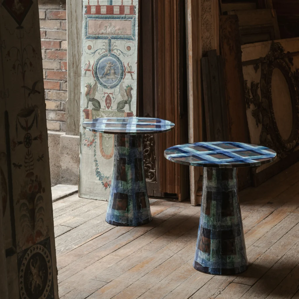 Pair of artistic blue patterned side tables with sculptural bases displayed in a rustic interior with antique painted panels.