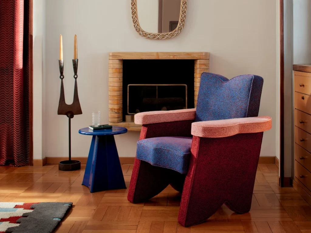 Bold modern armchair in blue and red upholstery with matching side table, styled in a retro-inspired living room with fireplace.