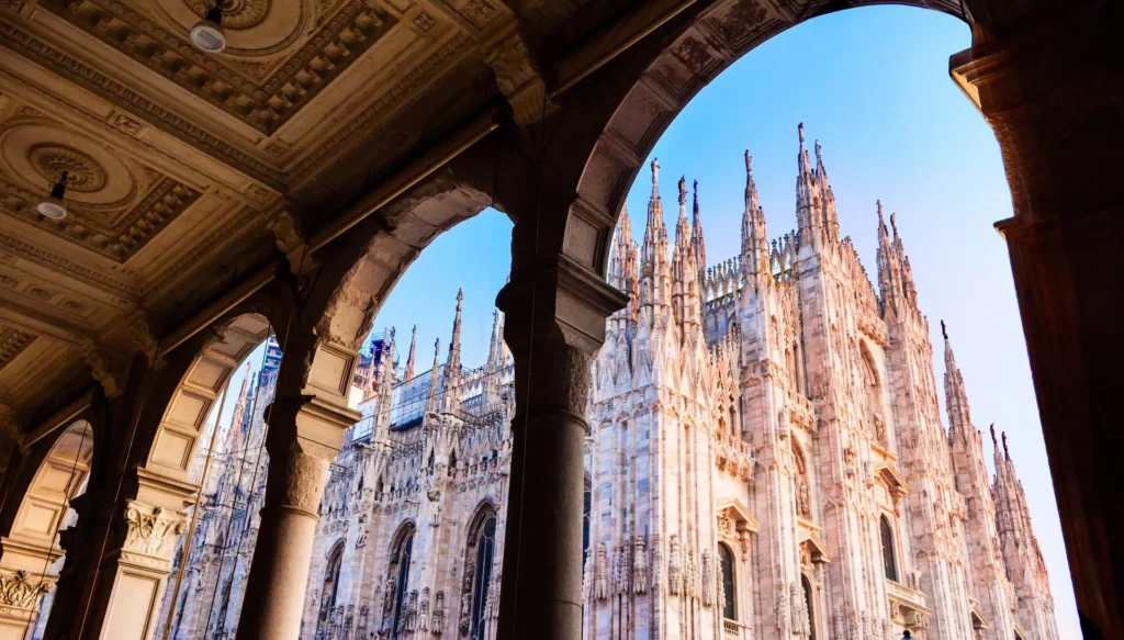Architectural view of Milan Cathedral (Duomo di Milano) framed by ornate stone arches and detailed ceilings.