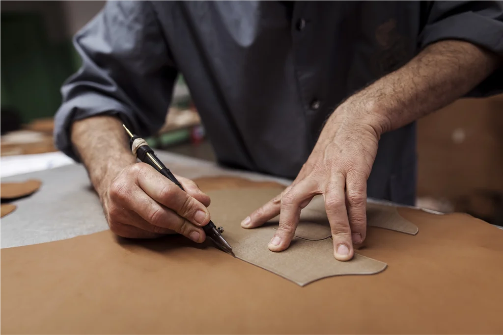 Craftsman’s hands carefully cutting leather using a template, showcasing traditional artisanal techniques in luxury craftsmanship