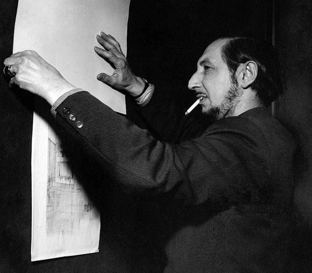 Black and white portrait of Italian architect Carlo Scarpa, holding architectural drawings.