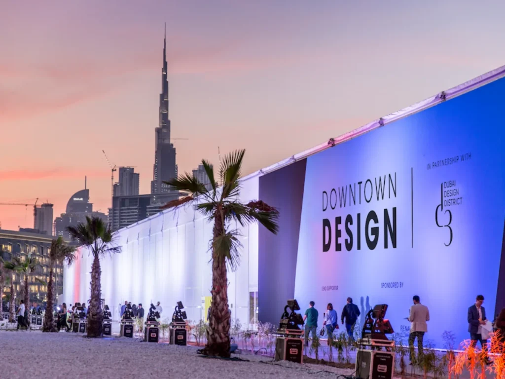 Dubai Design Week Downtown Design exhibition with Burj Khalifa skyline at sunset and illuminated pavilion.