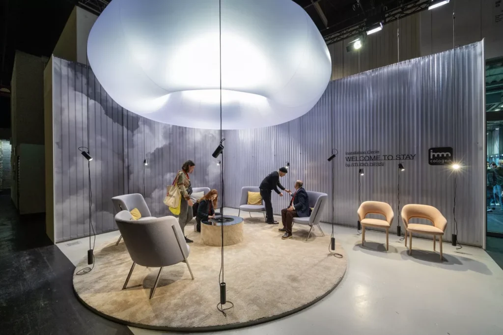 Installation at imm Cologne design fair featuring circular lounge with modern seating and illuminated ceiling display.