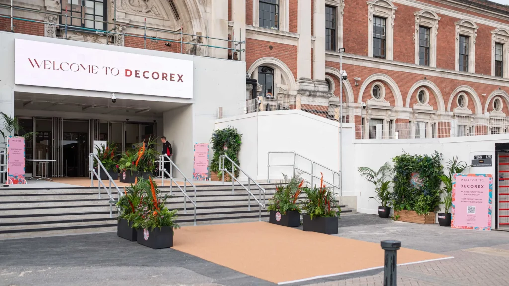 Entrance to Decorex International design fair in London with floral arrangements, signage, and historic architecture.