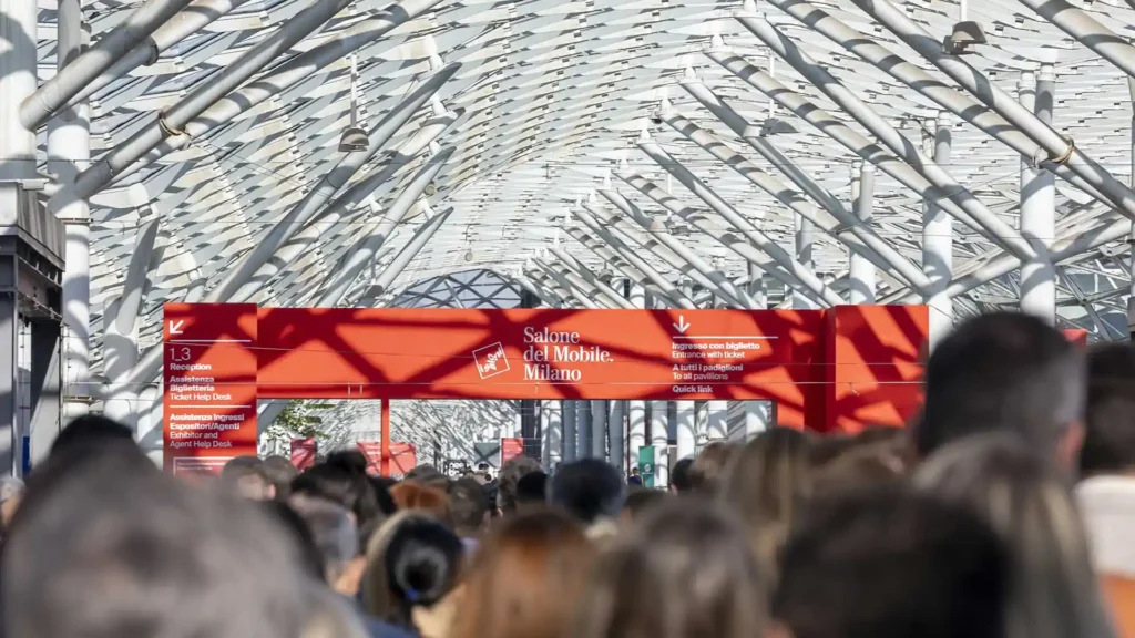 Crowds entering Salone del Mobile Milano under striking steel architecture and red signage.