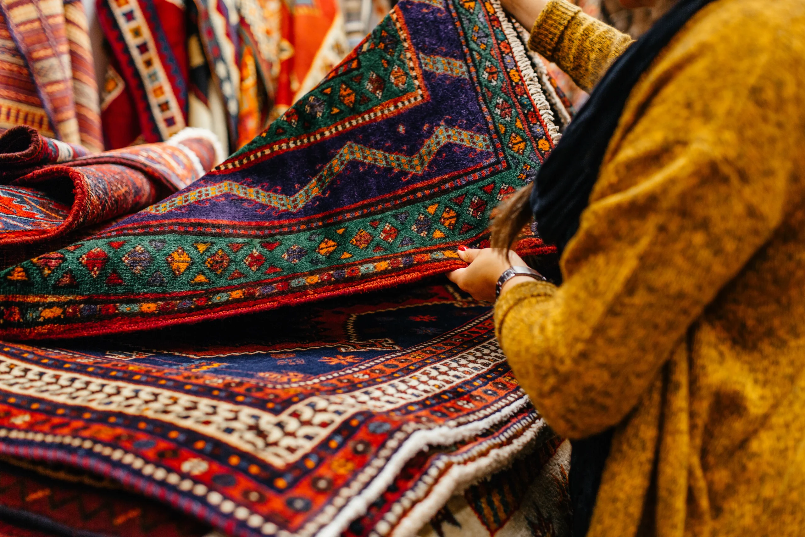 Close-up of a person examining a traditional handwoven Moroccan rug with vibrant geometric patterns.