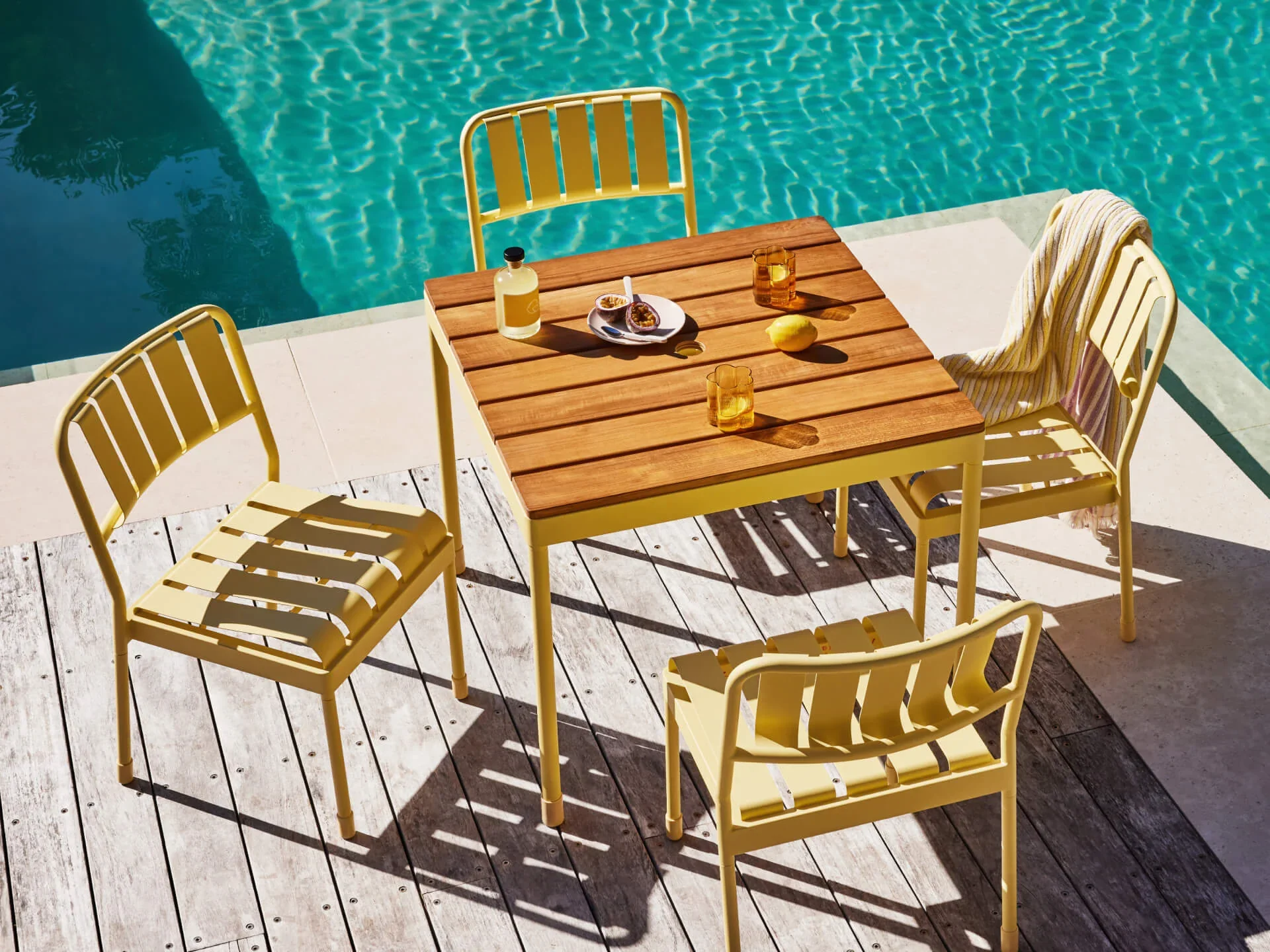 Modern yellow outdoor dining set with wooden tabletop beside a turquoise swimming pool.