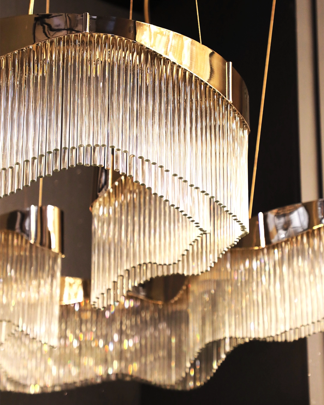 Luxury brass chandelier with sculptural curved design and cascading glass tubes by Castro Lighting.