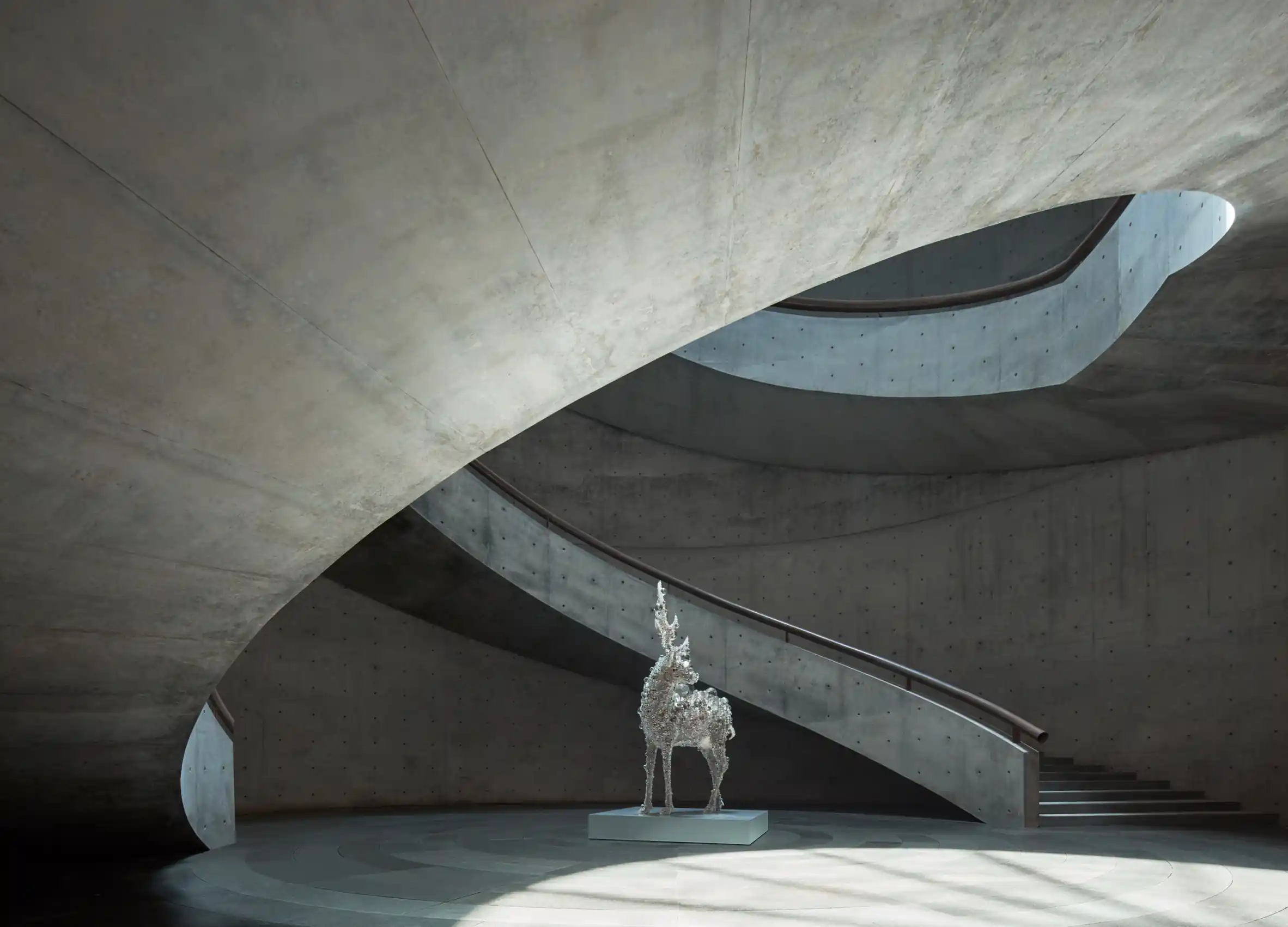 Minimalist concrete spiral staircase in a museum interior with sculptural lighting and art installation.