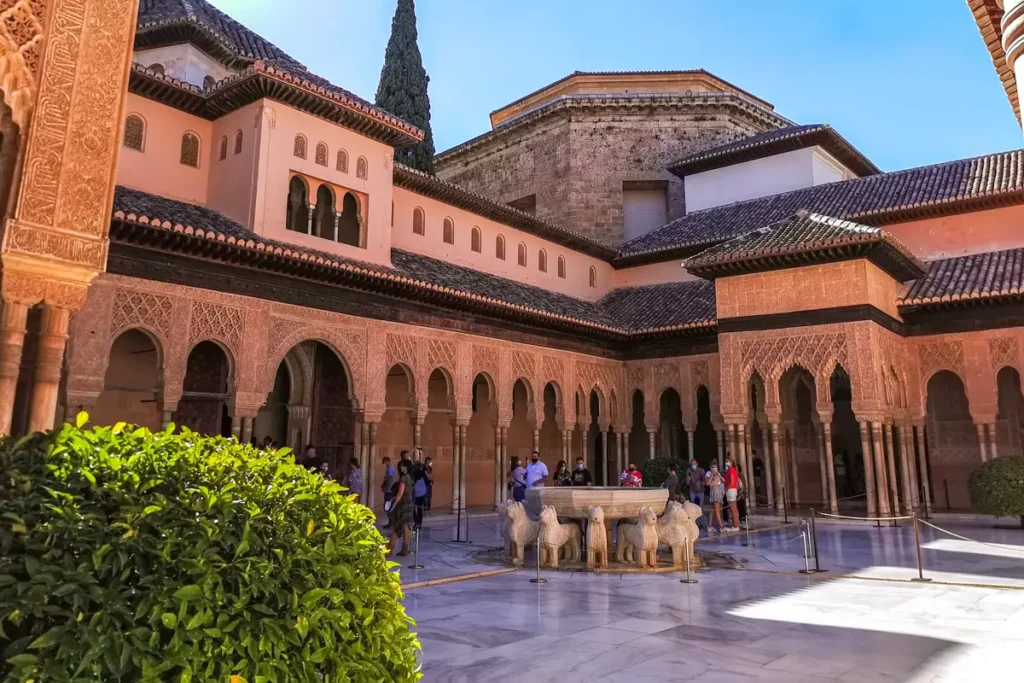 Moorish courtyard at the Alhambra in Granada featuring intricate stucco arches, marble flooring, and the iconic Fountain of the Lions under bright sunlight