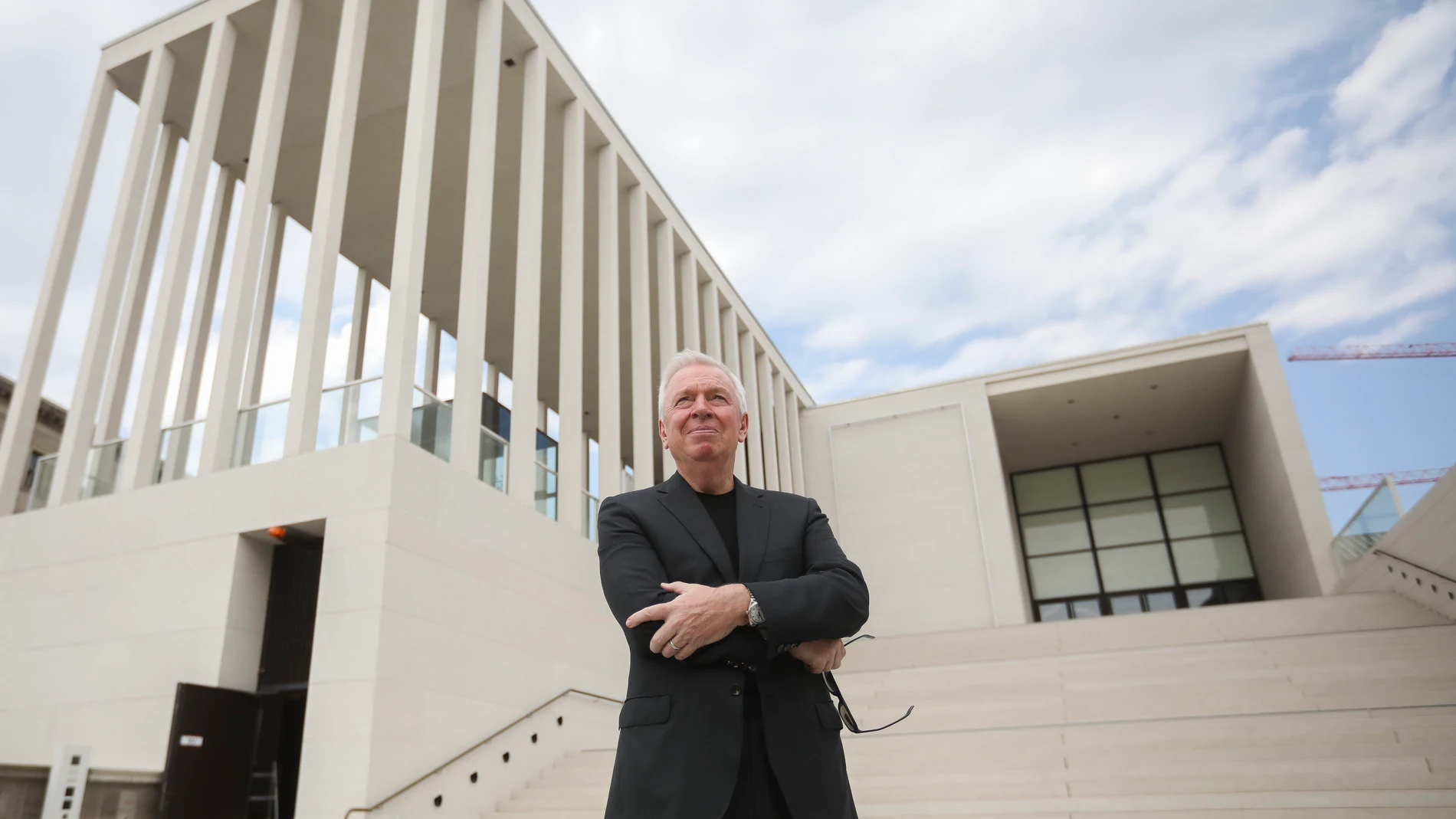 Contemporary architect standing before a minimalist concrete and glass building with vertical colonnades — a composition of modern European architecture, structural geometry, and design innovation.