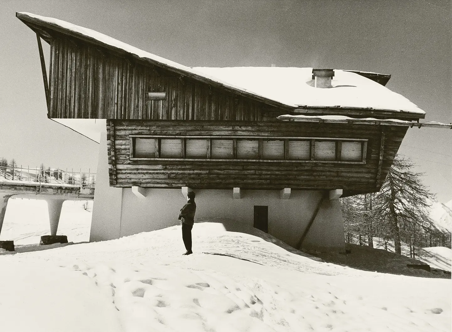 Snow-covered alpine chalet designed by Carlo Mollino, blending modernist structure with traditional mountain architecture.