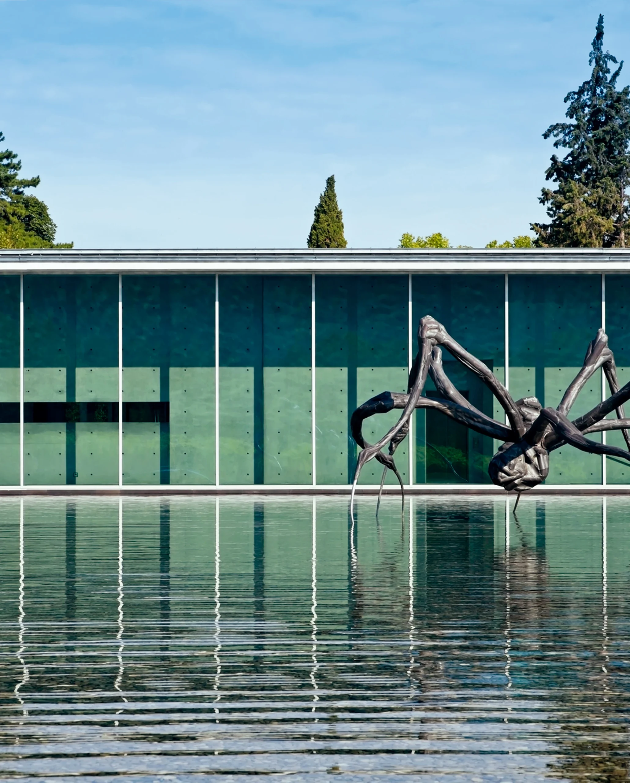 Modern art museum with green facade reflected in water, featuring large abstract outdoor sculpture