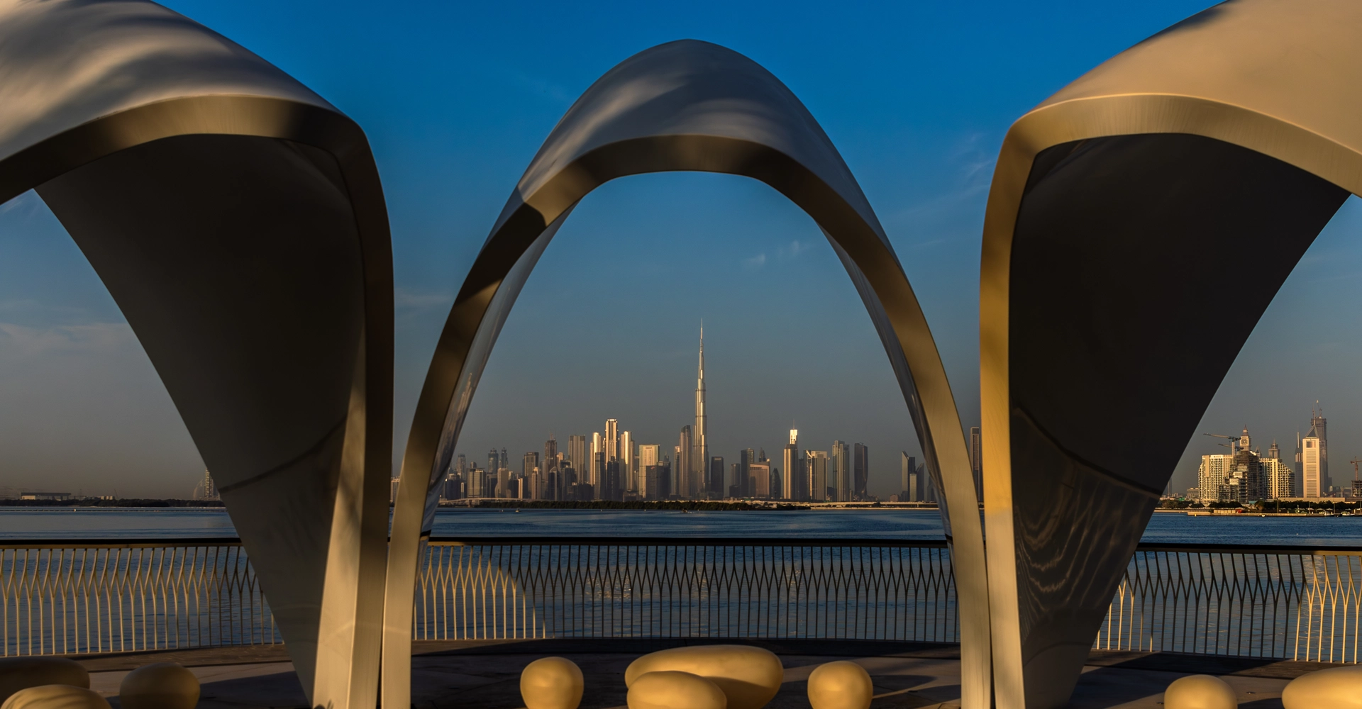 View of the Dubai skyline framed by modern architectural arches, with the Burj Khalifa in the distance.