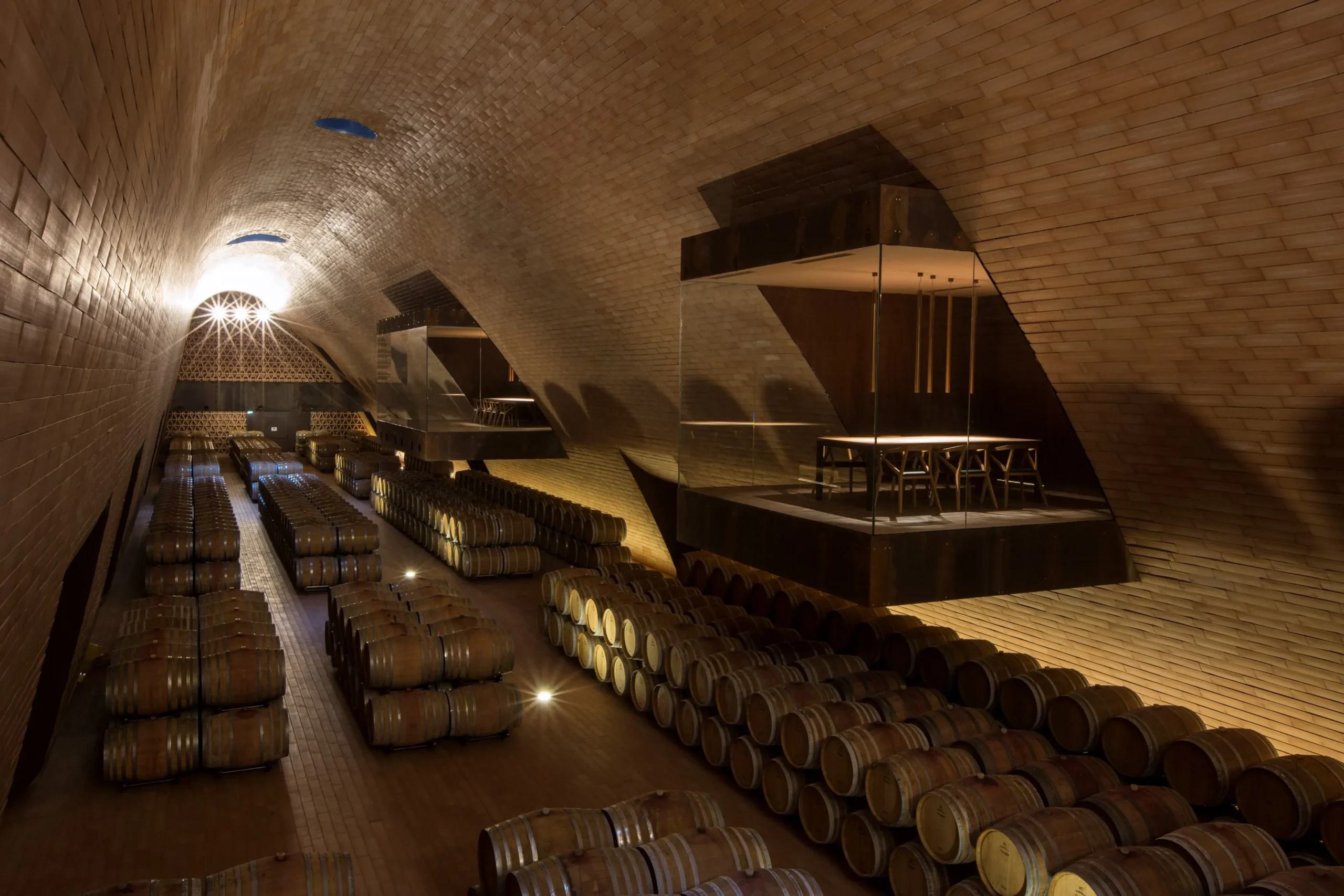 Architectural wine cellar with vaulted brick ceilings and ambient lighting illuminating rows of oak barrels