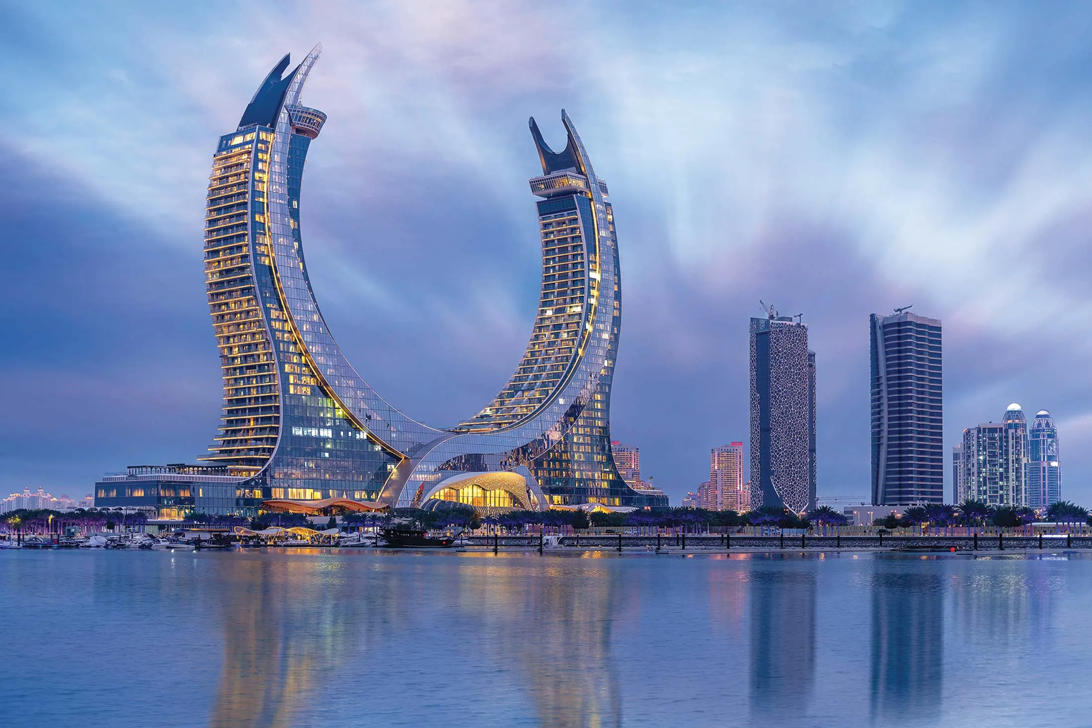 Striking twin-arched Katara Towers in Lusail, Qatar, rising over the waterfront skyline at dusk.