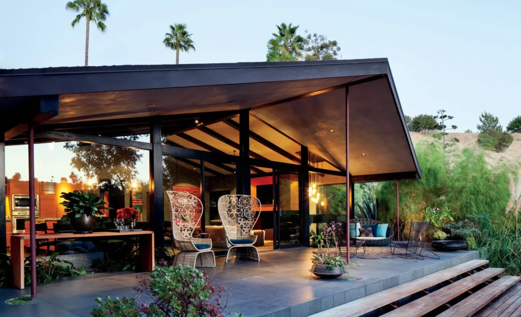Mid-century modern home in California with glass walls, slanted roof, and outdoor lounge surrounded by greenery.