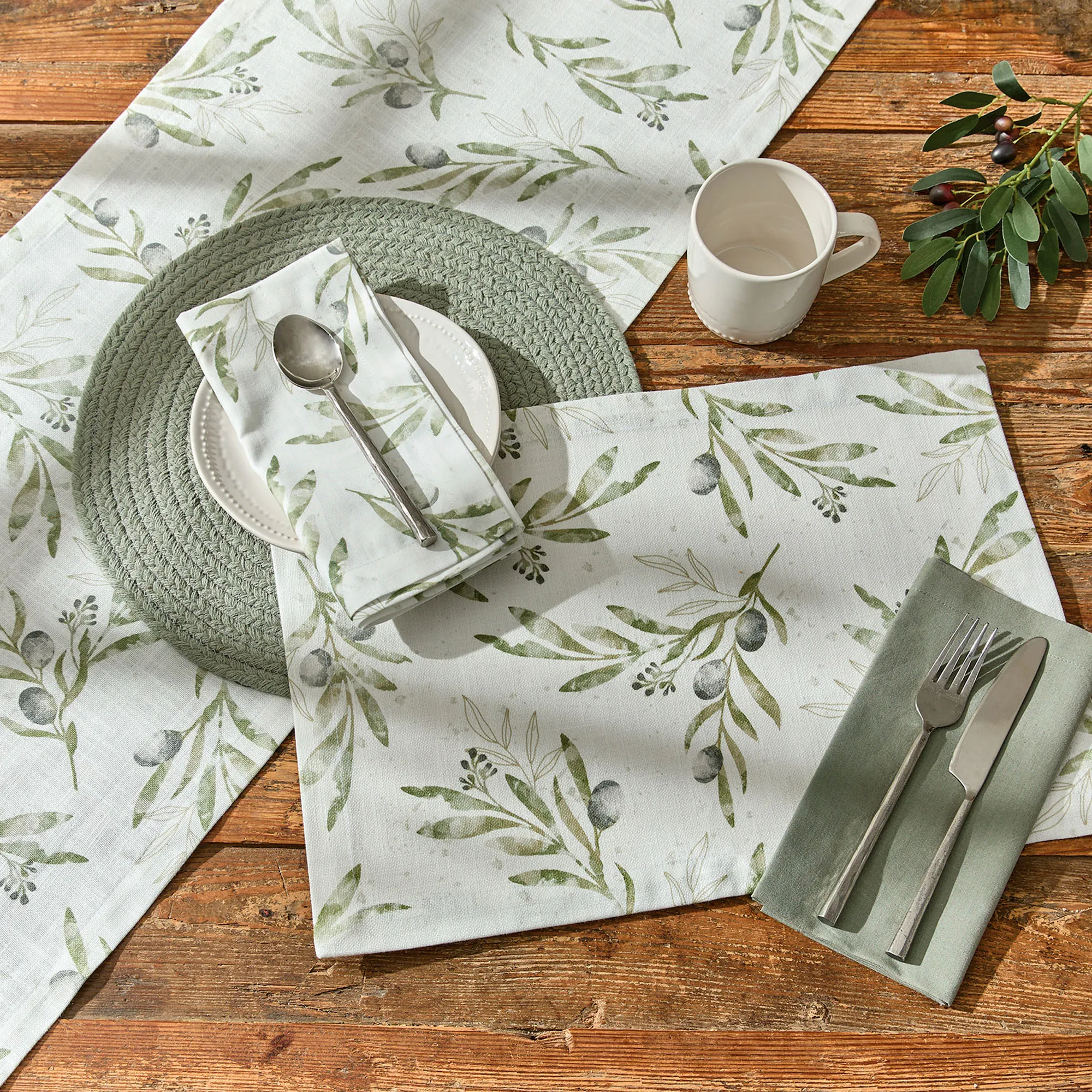 Mediterranean-inspired table setting with olive branch printed linens, rustic wood table, and ceramic dishware.