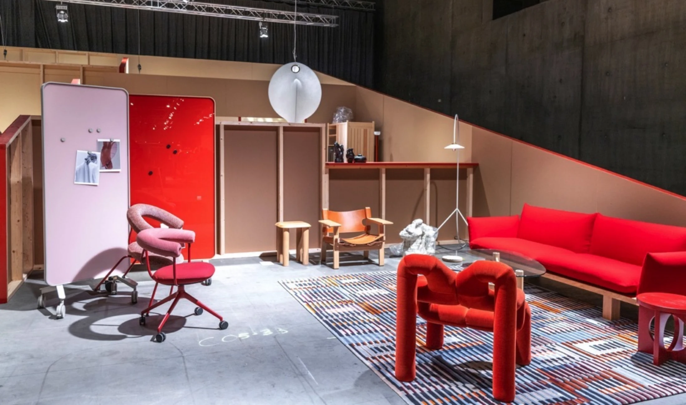 Oslo Design Fair exhibition featuring contemporary furniture, red seating, wooden structures, and a patterned rug.
