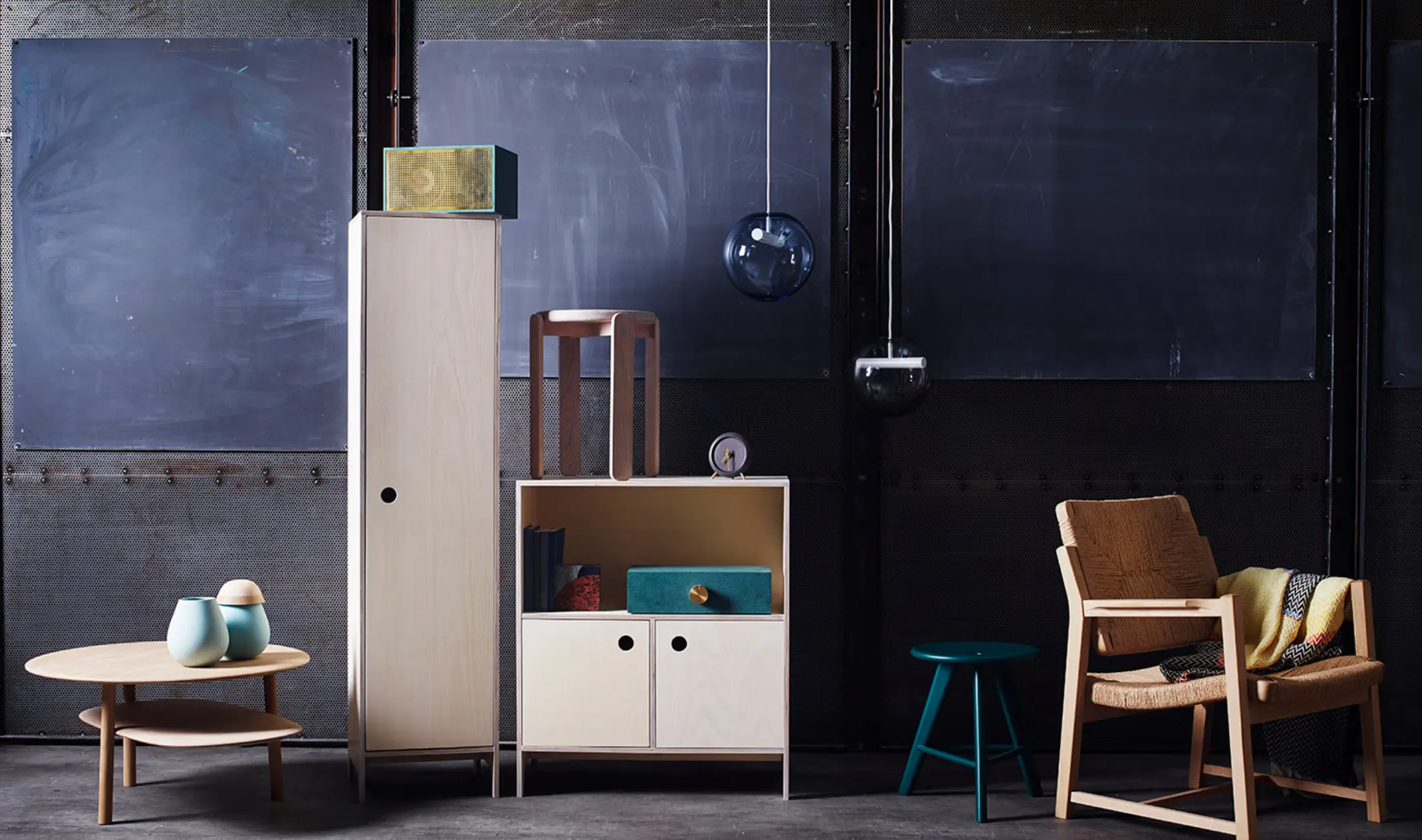 Contemporary furniture exhibition with wooden seating, cabinets, tables, and lighting against a dark backdrop.