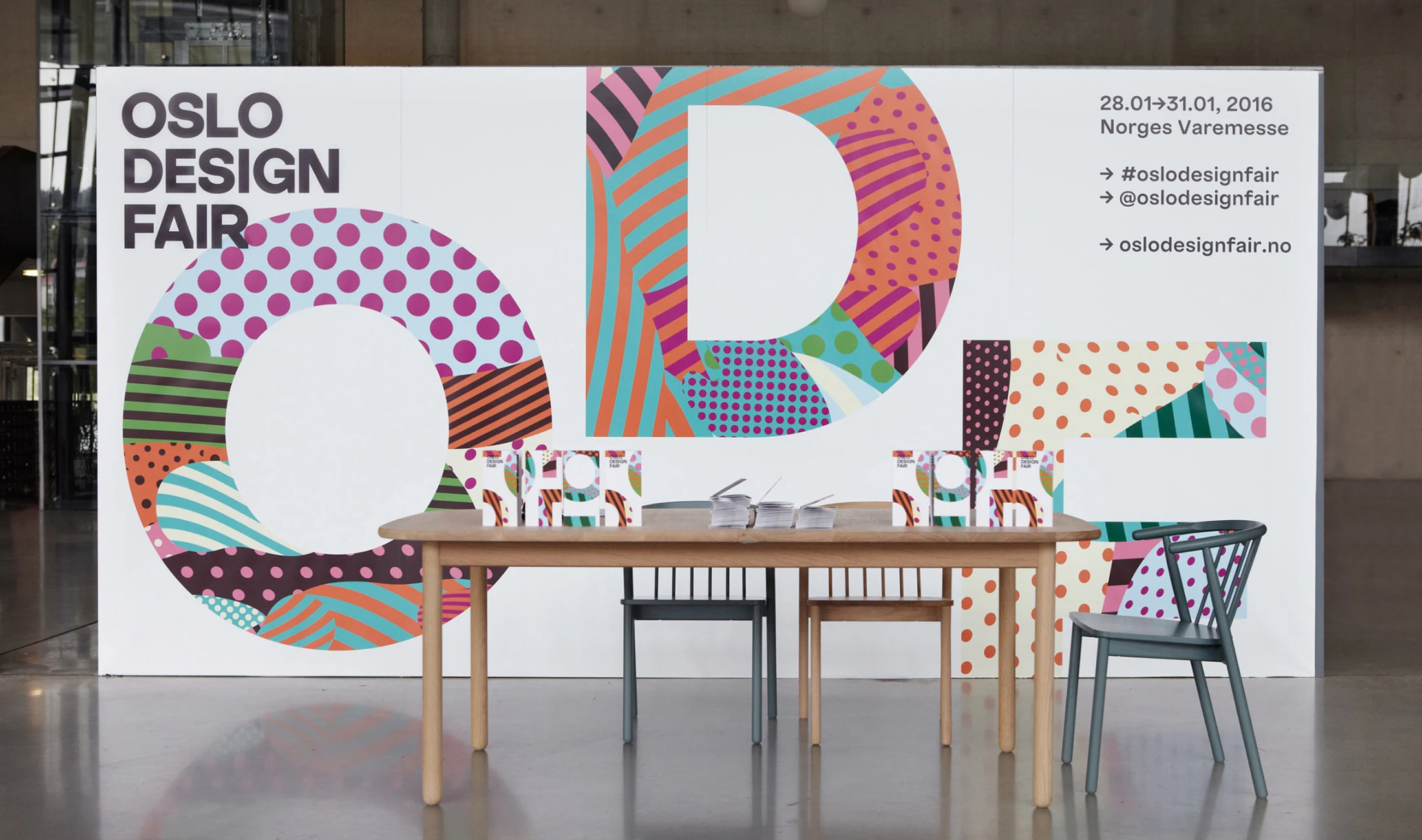 Oslo Design Fair entrance table displaying event flyers against a colourful geometric backdrop.