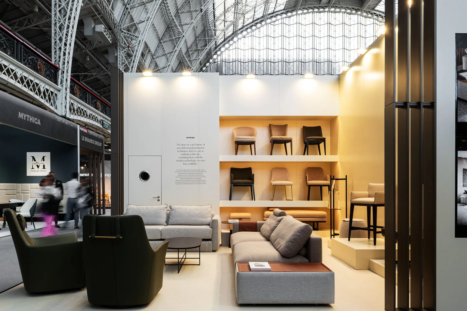 Domkapa’s exhibition booth at Decorex 2023, Olympia London, featuring contemporary upholstered chairs and sofas in neutral tones under the venue’s iconic glass and steel roof. The display highlights craftsmanship and modern design within the international furniture fair.