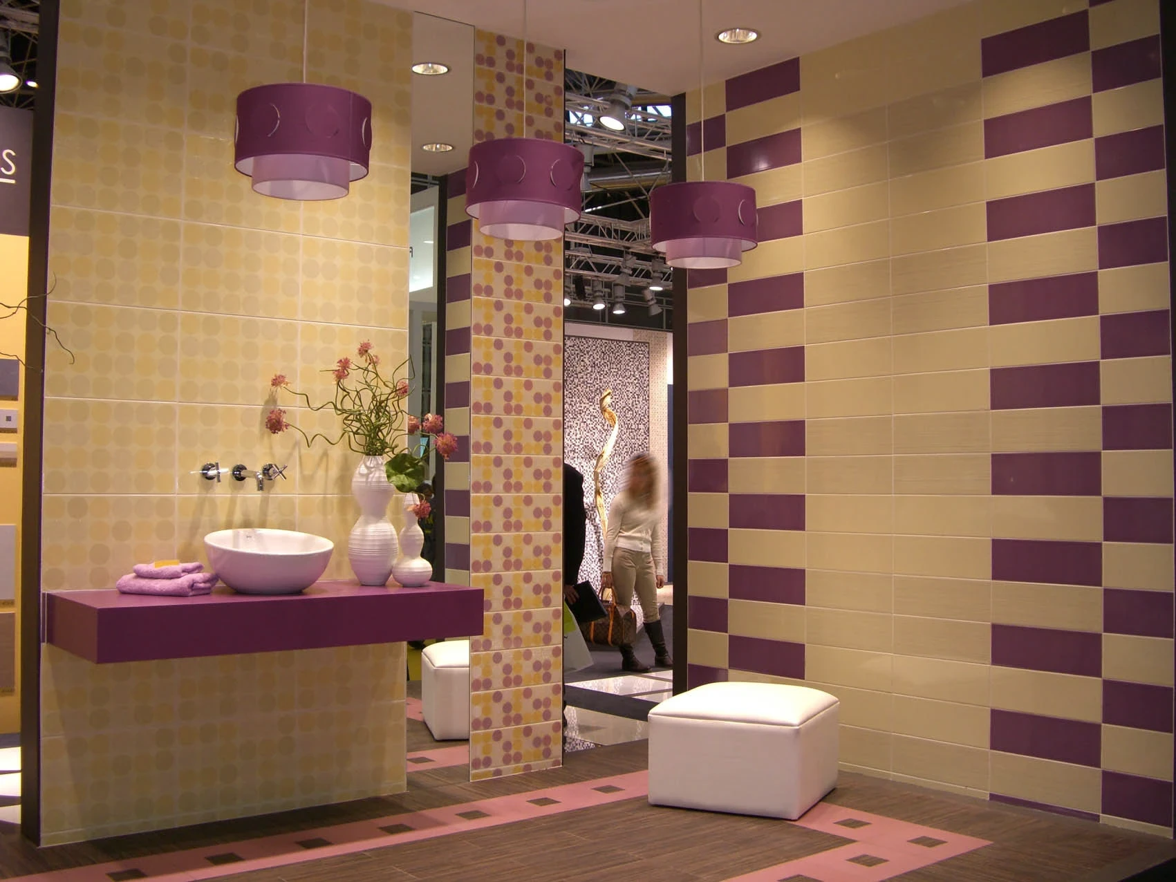 Bathroom exhibition display featuring cream and purple wall tiles, matching pendant lamps, a floating purple vanity, and a white vessel sink.