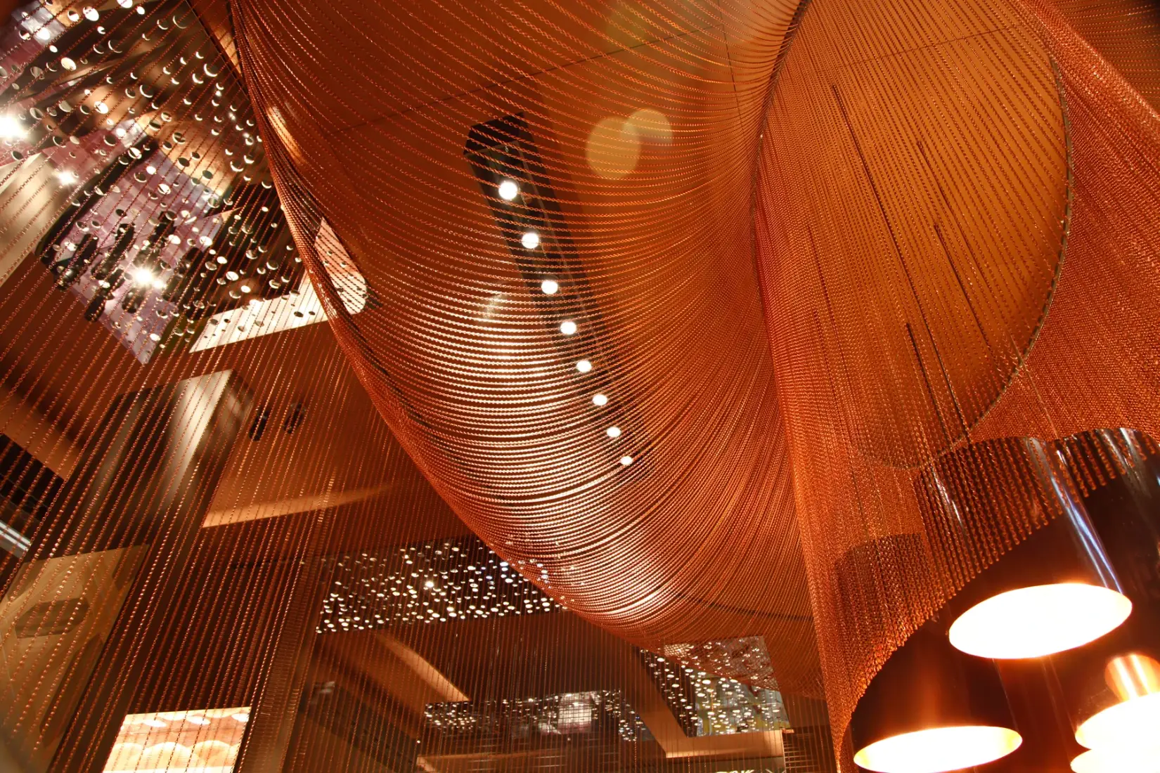 Copper colored chains draped in sweeping curves above pendant lights at Royal Ceramica’s Cevisama 2012 stand.