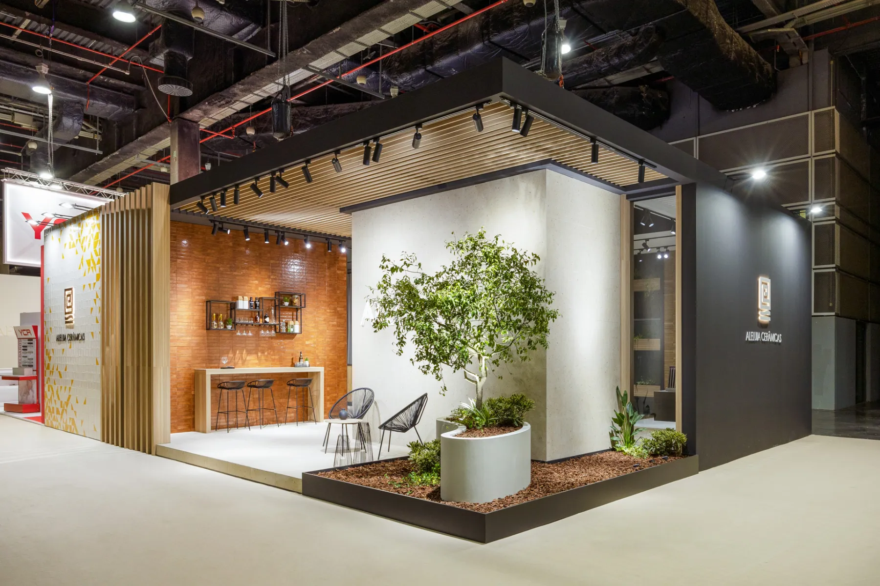 Aleluia Cerâmicas stand at Cevisama 2024, featuring terracotta-colored tiles, pale wall surfaces, wood slats, and planted seating areas.