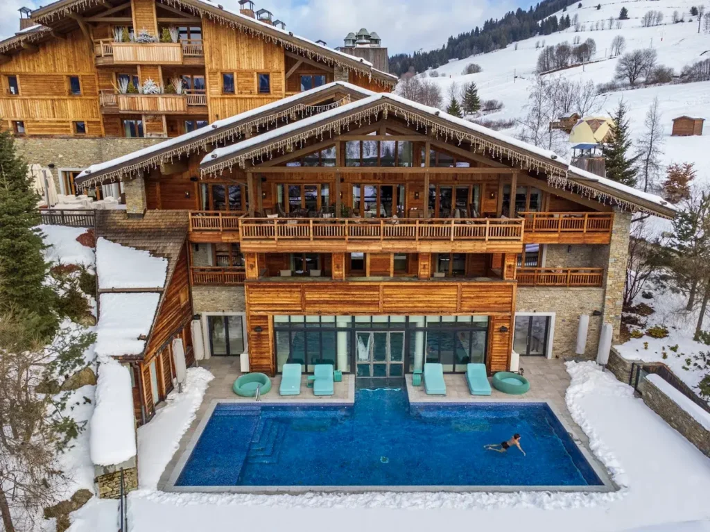 Four Seasons Resort Megève with timber chalet architecture, heated outdoor swimming pool and snow-covered mountain slopes in France.